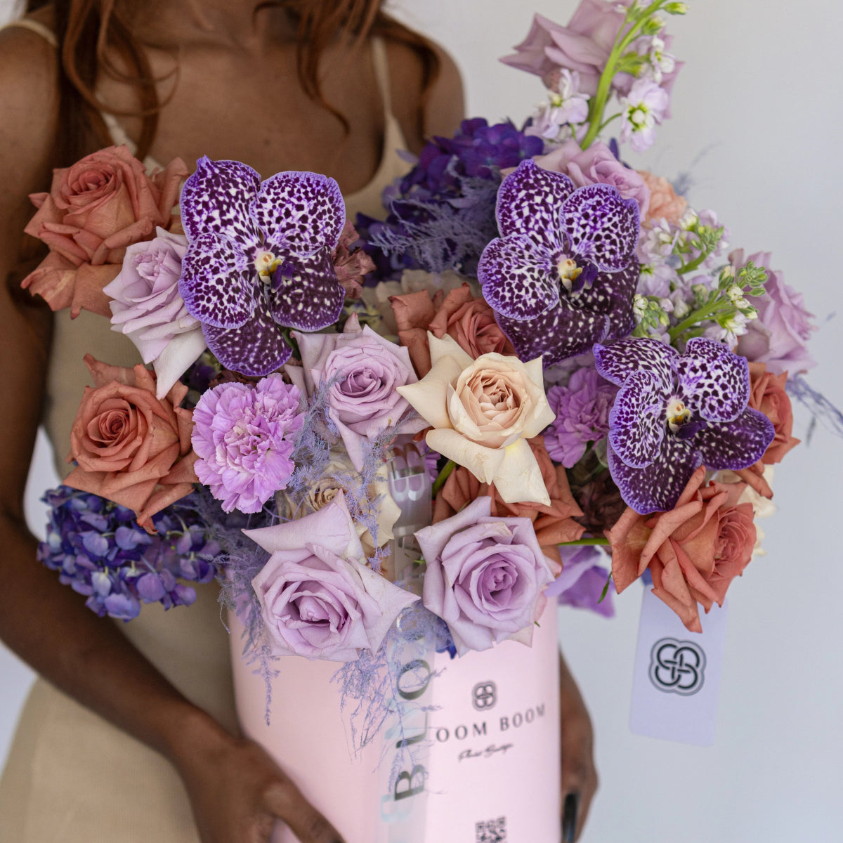 Luxury pink box filled with purple spotted orchids, coral roses, lavender roses, and purple carnations bouquet