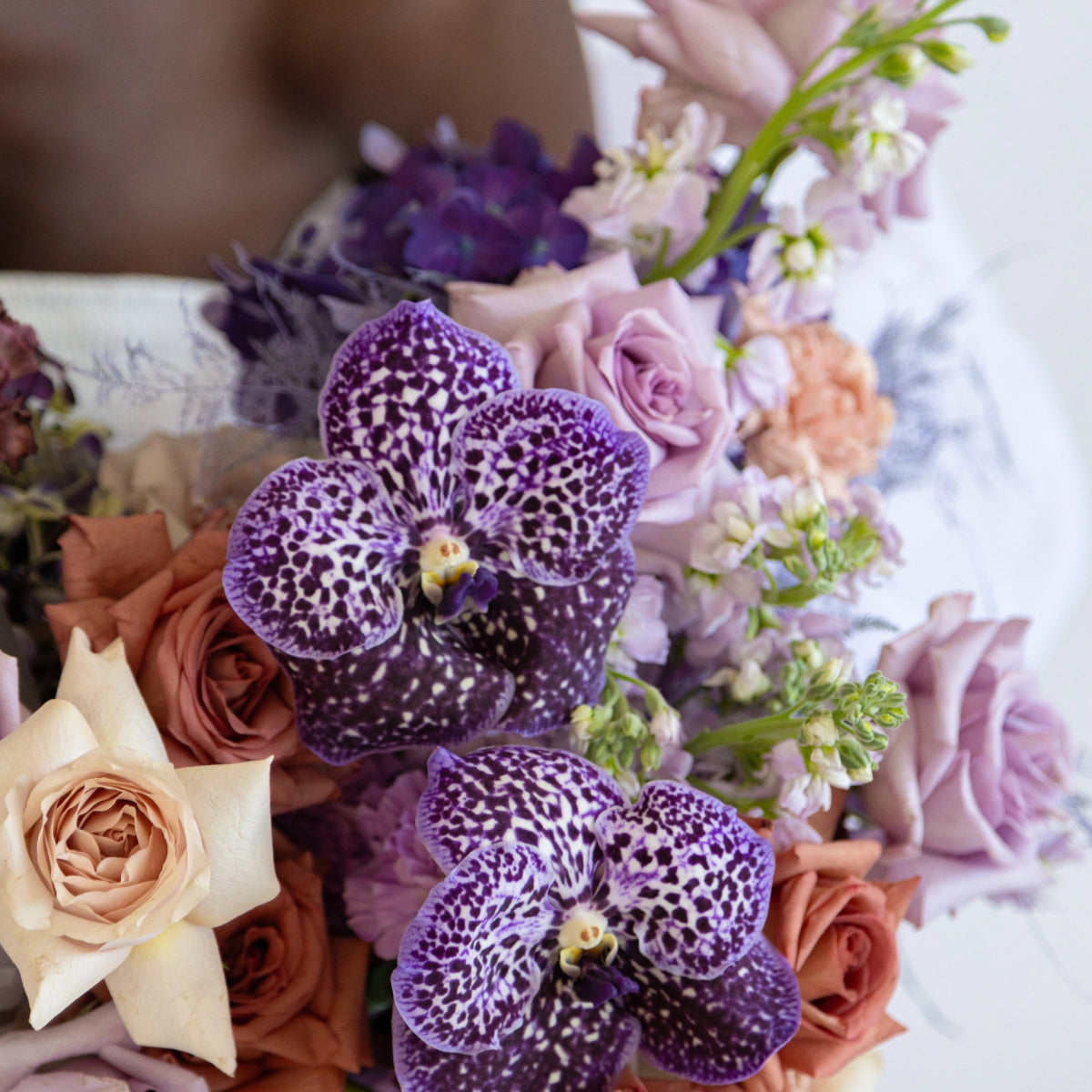 Purple spotted orchids with peach roses and lavender flowers in elegant mixed bouquet arrangement