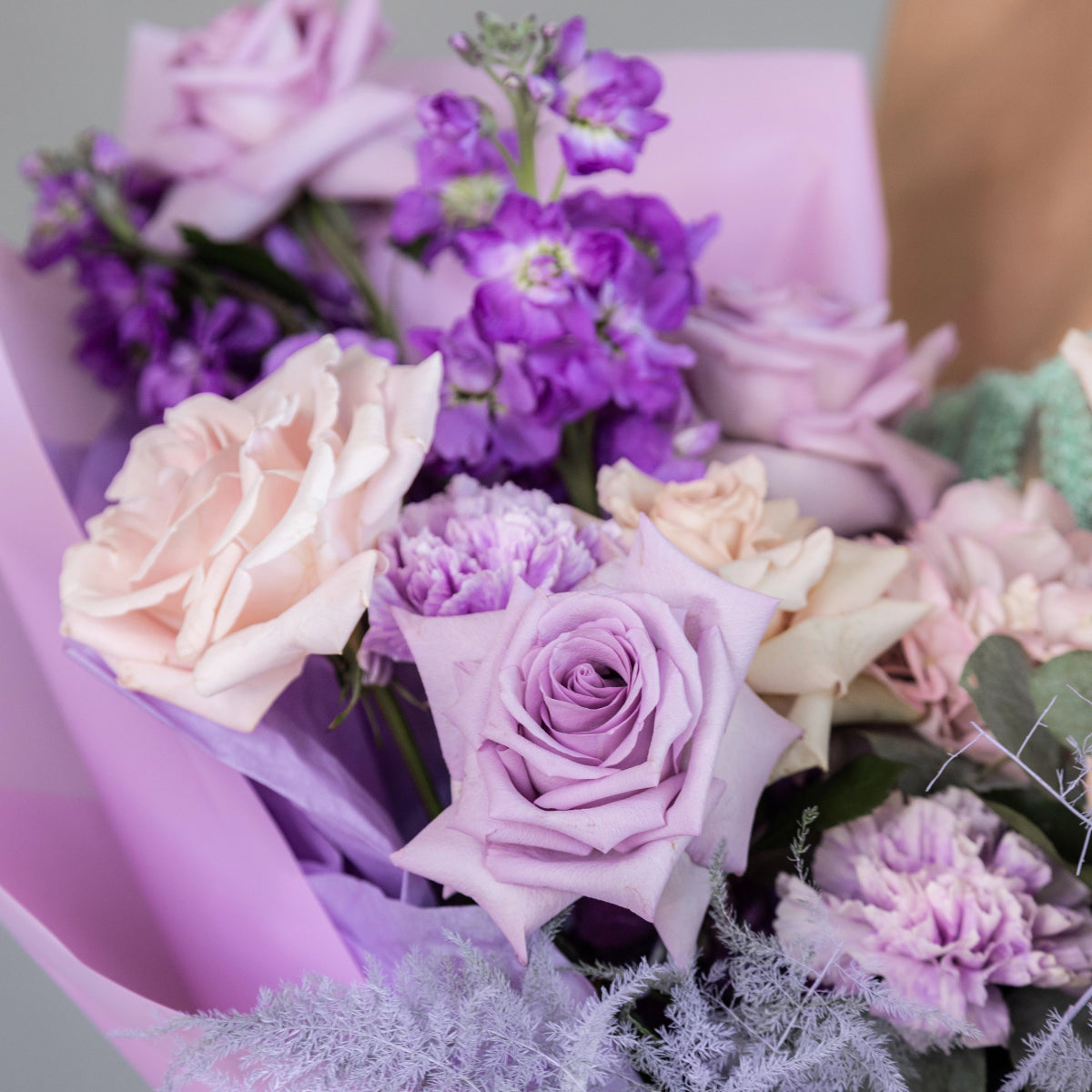 Purple and pink flower bouquet with lavender roses, carnations, and stock flowers wrapped in lilac paper