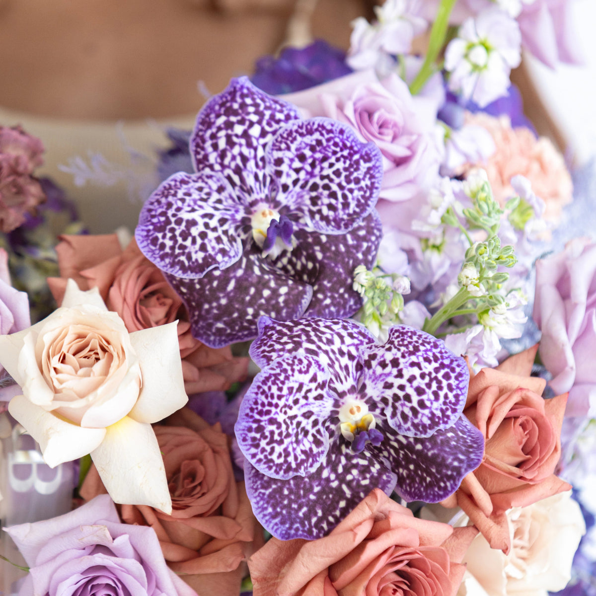 Purple spotted orchids with peach roses and lavender flowers in mixed floral arrangement bouquet