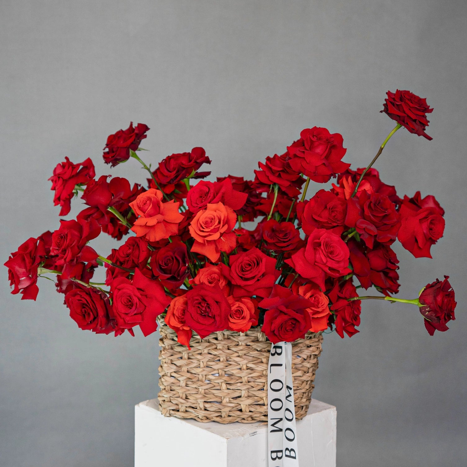 Red and coral roses arranged in woven wicker basket with Bloom Boom Flowers ribbon - premium rose delivery Los Angeles