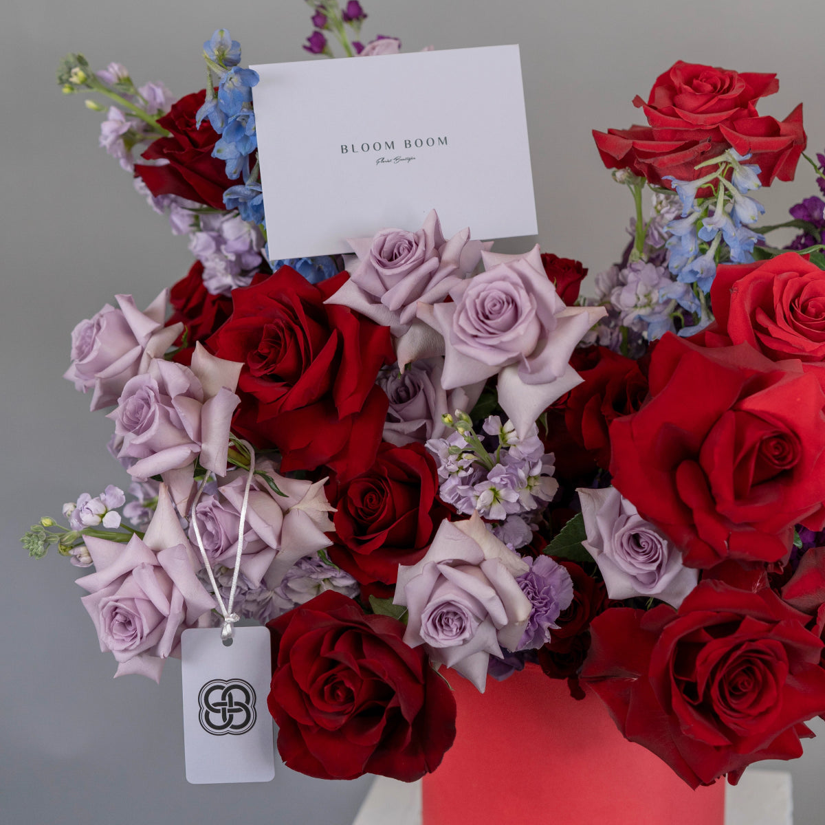 Mixed rose bouquet with red and lavender roses, purple stock flowers, and Bloom Boom branded white gift card