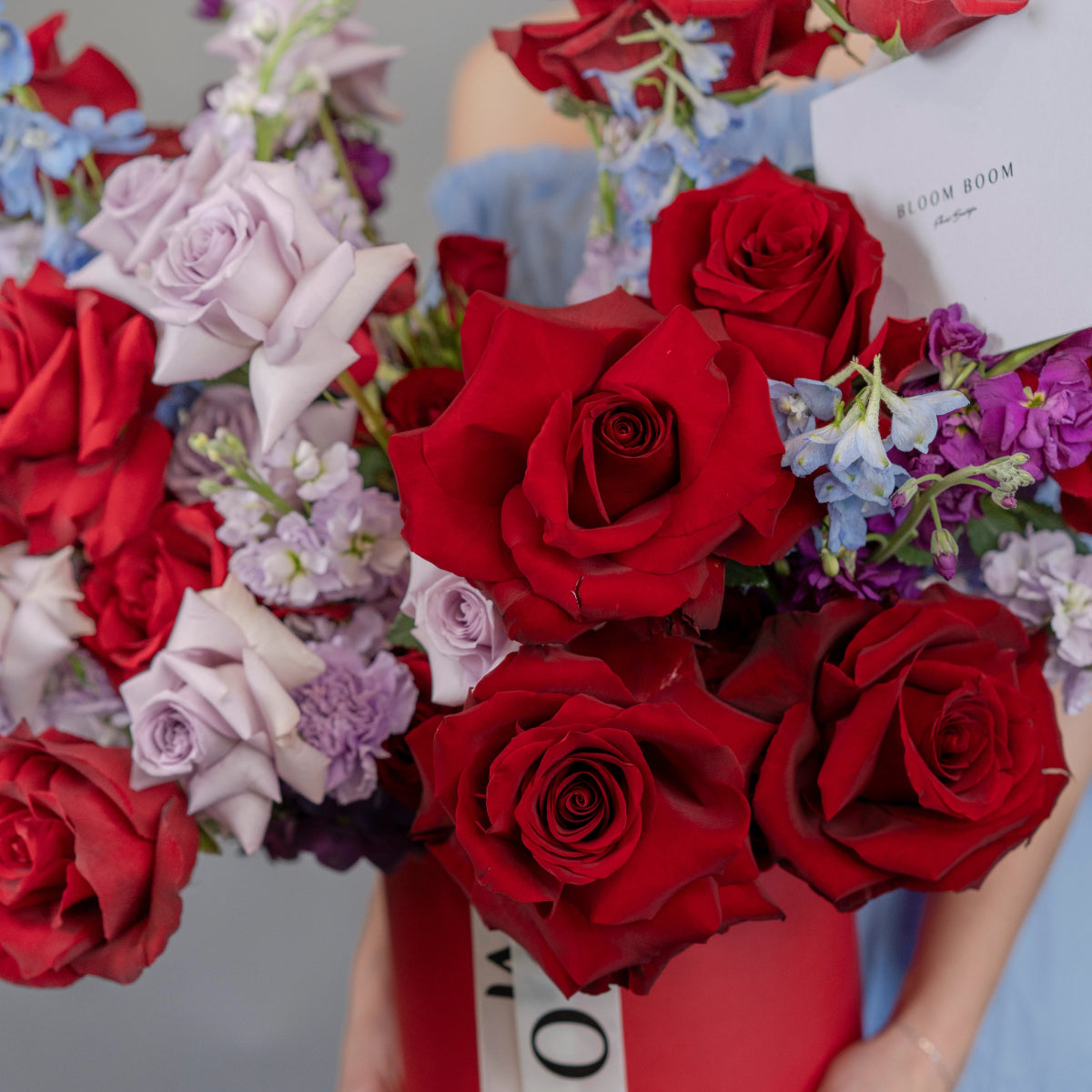 Red roses, lavender roses and purple flowers arranged in white gift box with Bloom Room branding