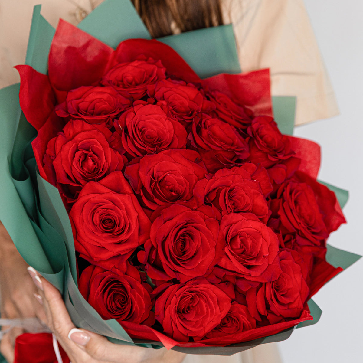 Fresh red rose bouquet wrapped in sage green paper with red ribbon held by woman in cream sweater