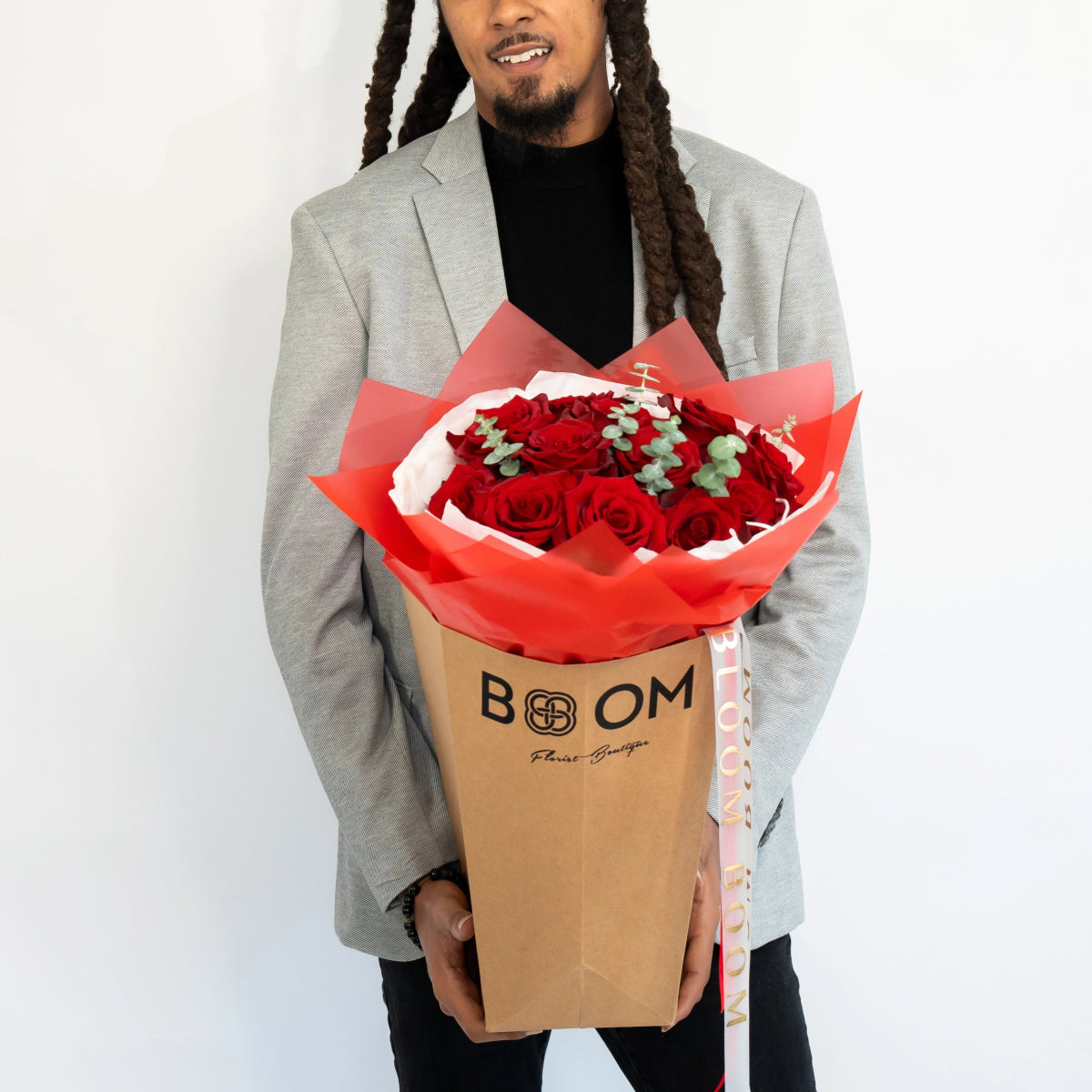Red roses bouquet in coral tissue paper and tan BOOM branded kraft box held by man in gray blazer