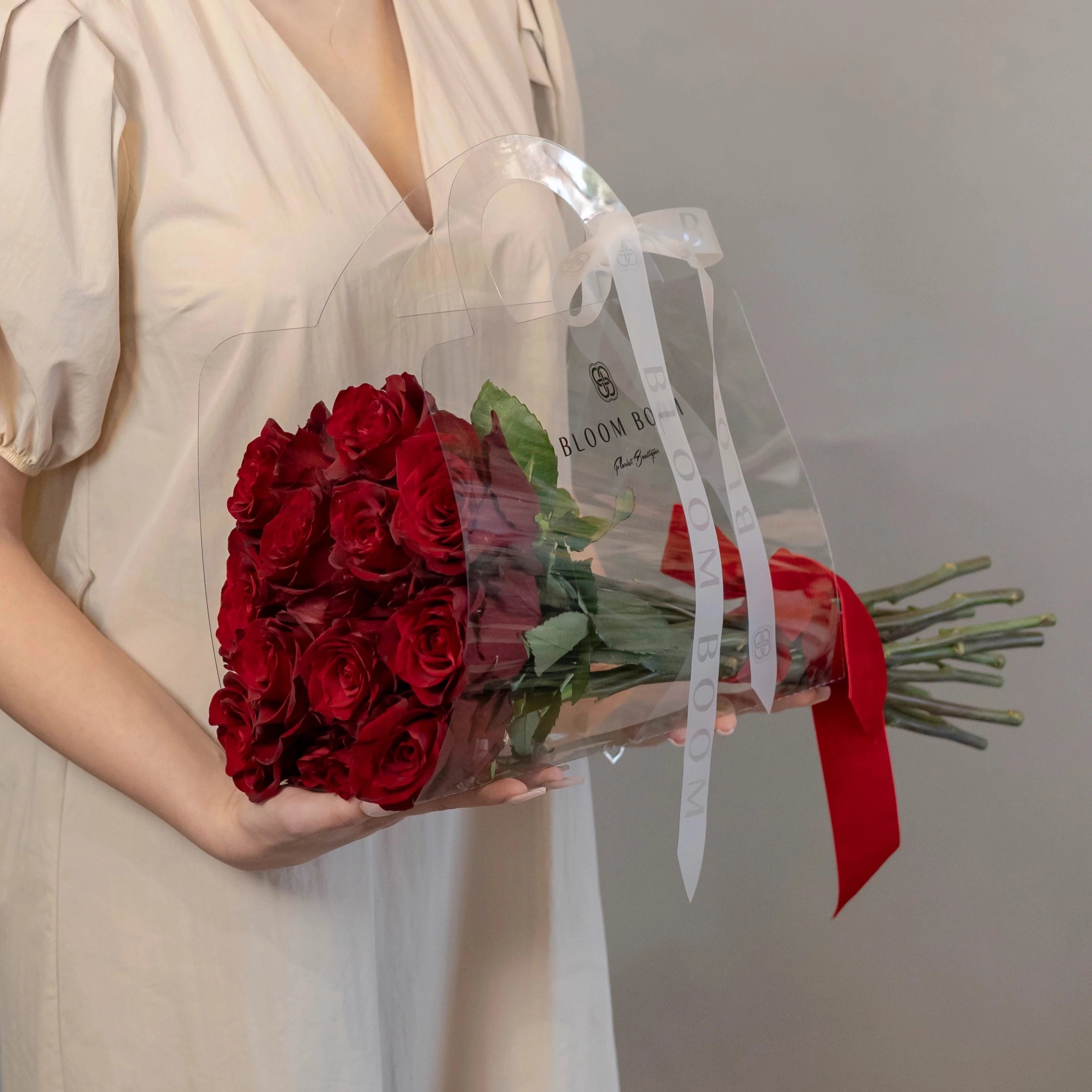 Deep red roses bouquet in transparent gift bag with Bloom Boom branding and red ribbon, perfect for romantic gifts