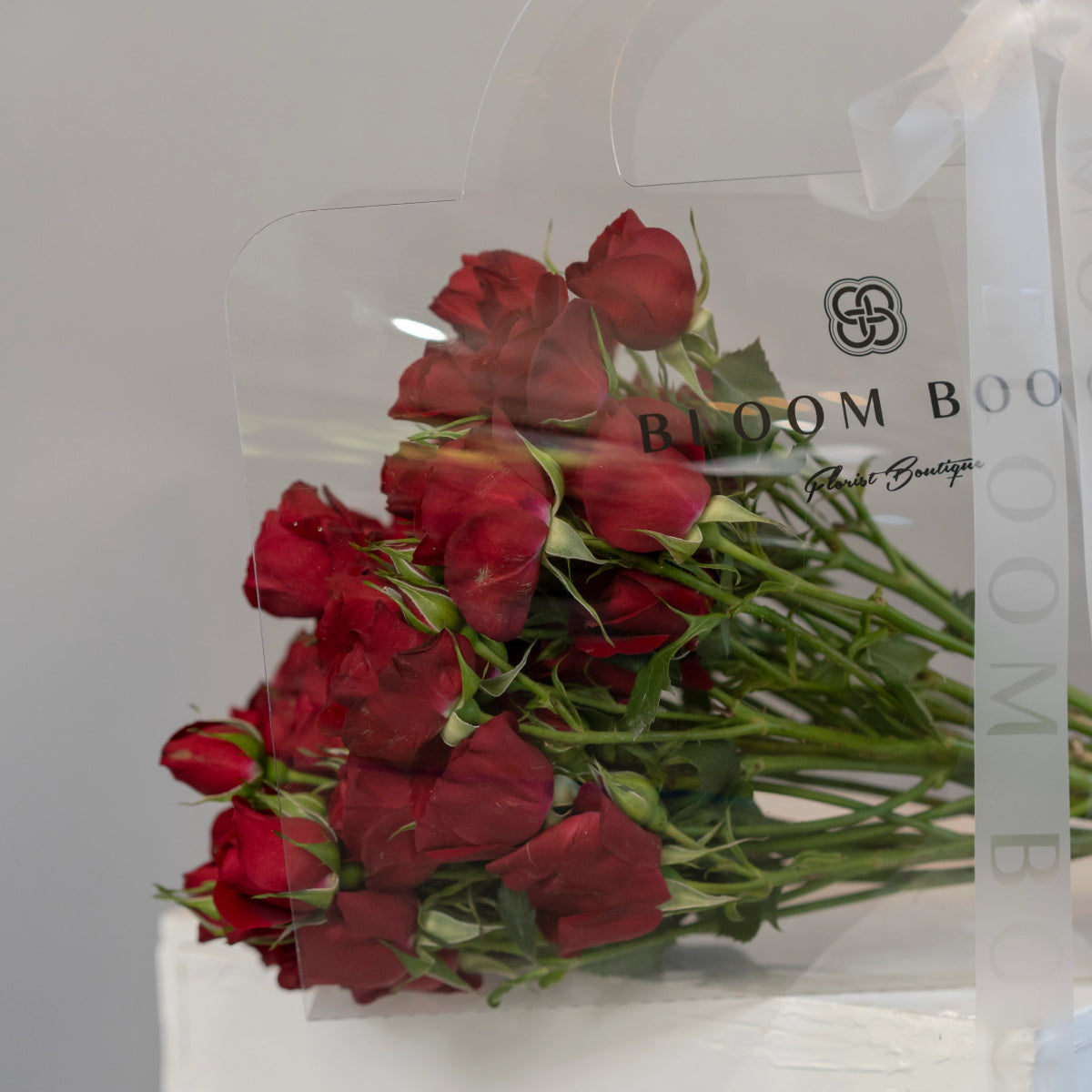 Dozen red spray roses with green stems in clear water tube packaging from Bloom Box Florist Boutique