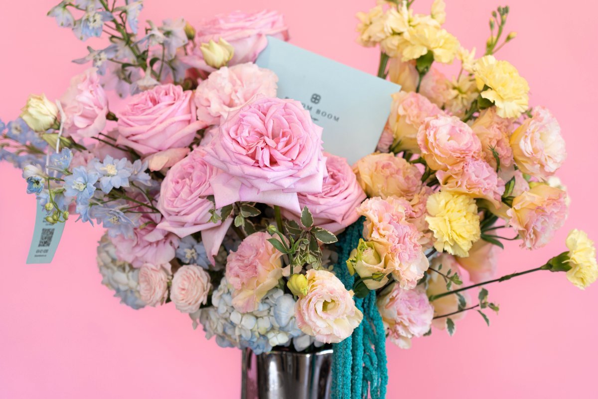 Mixed spring bouquet with pink roses, yellow carnations, blue delphinium in glass vase tied with teal ribbon