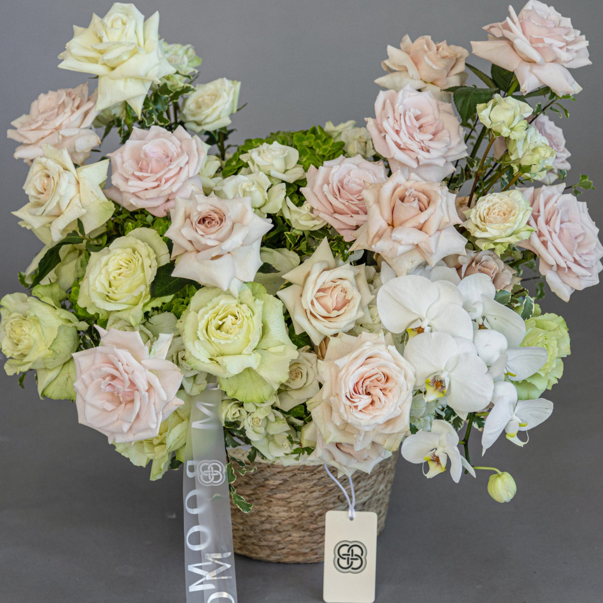 Elegant flower basket with blush pink and cream roses, white orchids, and green hydrangeas in woven basket