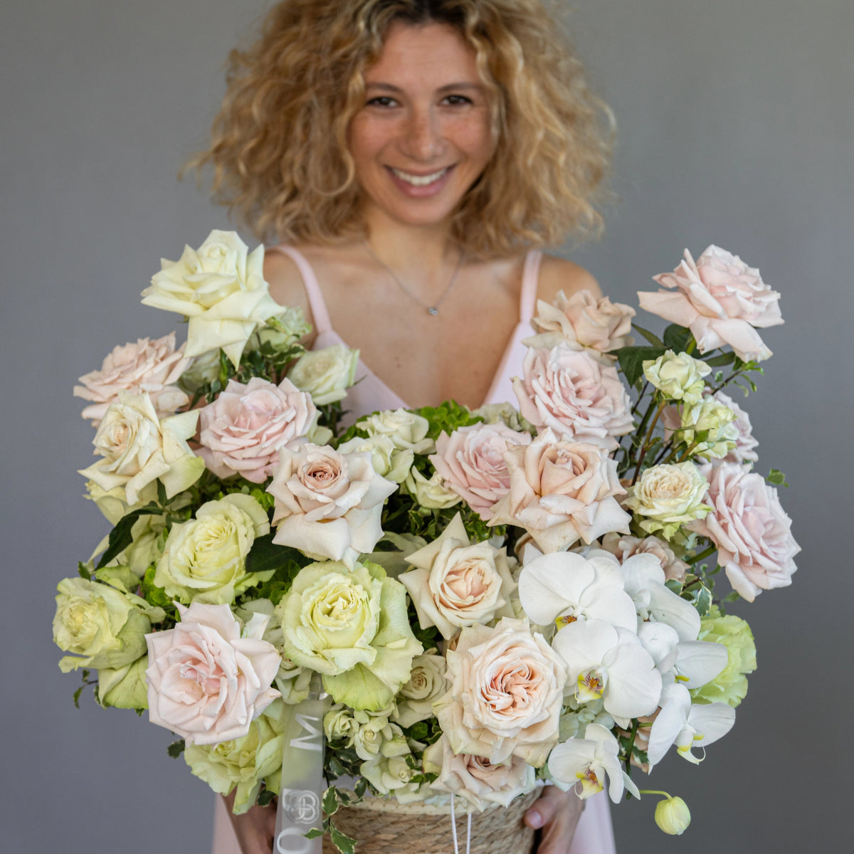 Sweet Lemonade flower basket with pink roses, white orchids, green hydrangeas in woven basket held by smiling woman