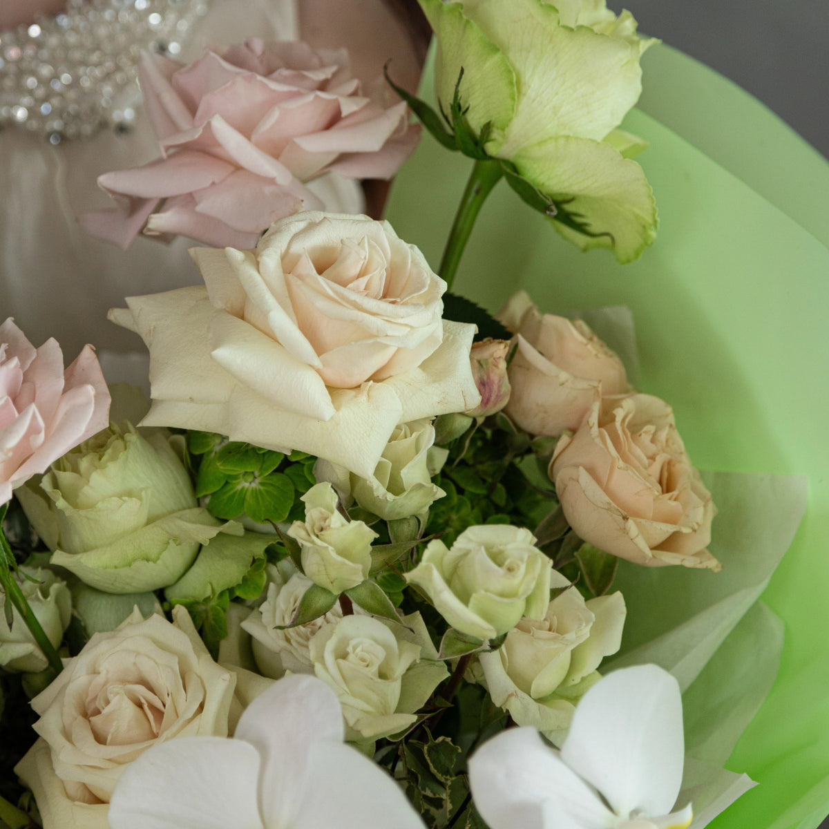 Mixed flower bouquet with cream roses, pink blooms, white orchids and green ribbon wrapping