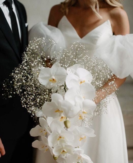White orchid bridal bouquet with baby's breath and crystal accents held by bride in strapless gown