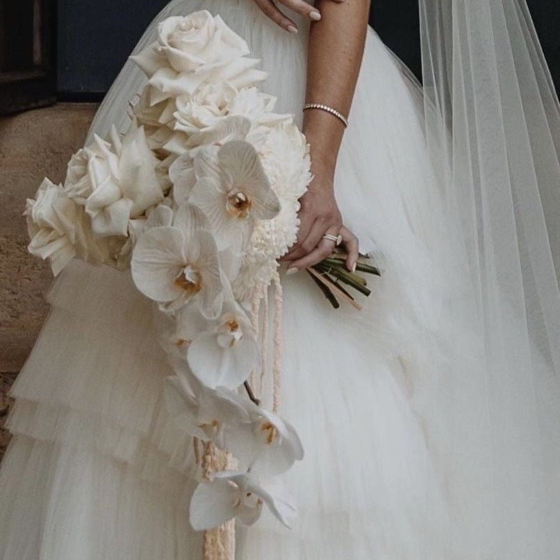 Elegant white orchid and rose bridal bouquet with pearl bracelet against flowing ivory wedding dress