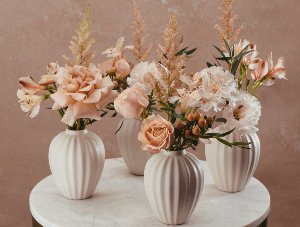 Three white ribbed ceramic vases with blush pink roses, white alstroemeria, and golden astilbe on marble table