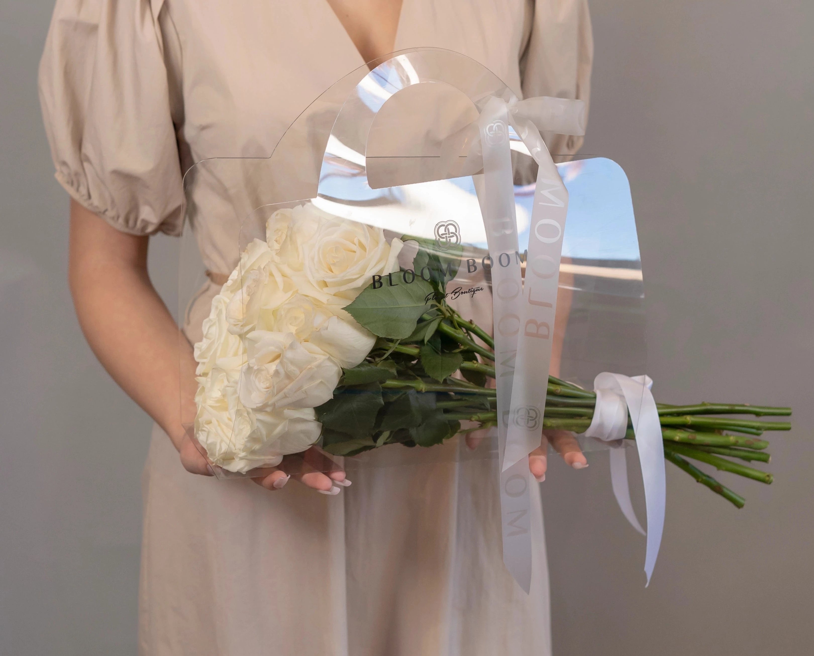White rose bouquet in clear Bloom Boom gift bag with ribbon ties, perfect for elegant flower delivery
