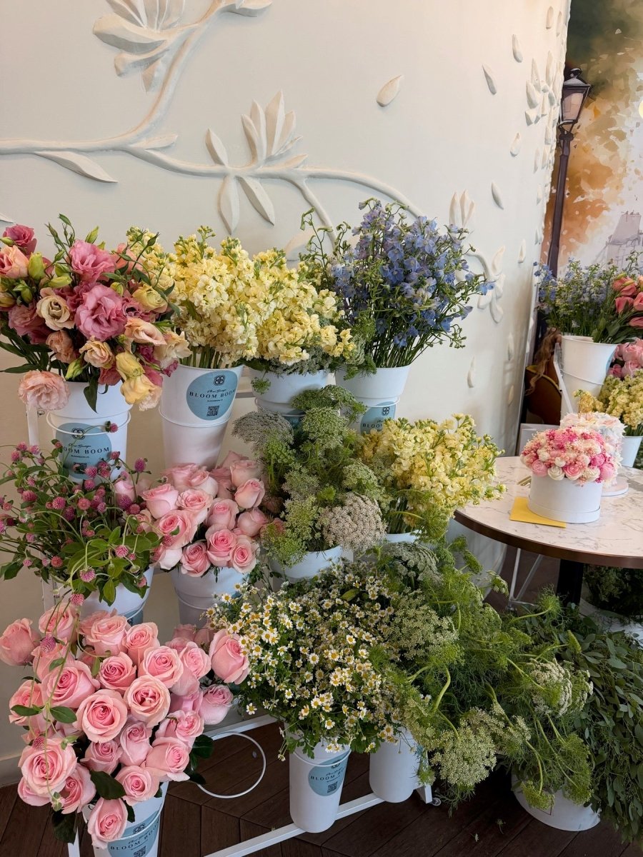 Lush flower bar with pink roses, cream stock, and blue delphinium in Bloom Boom buckets.