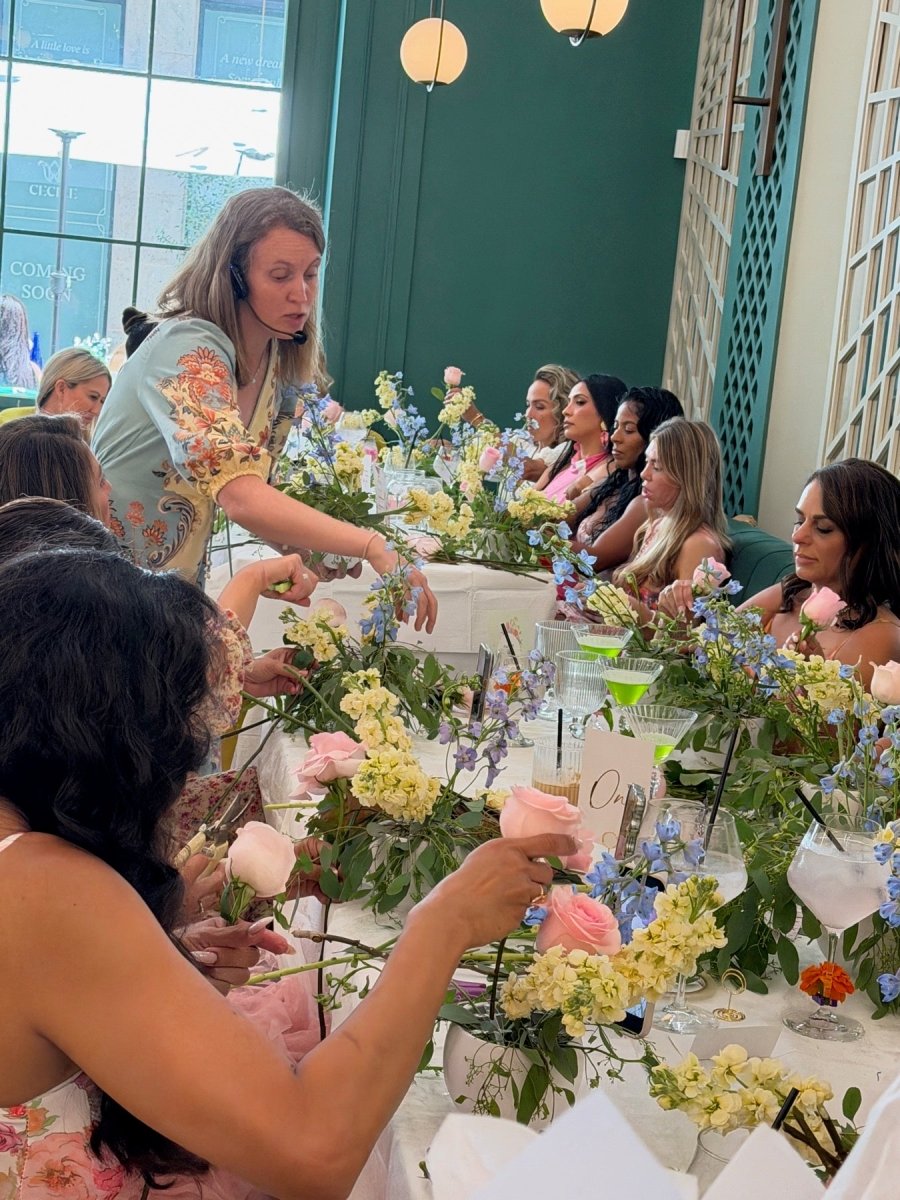 Bloom Boom instructor with a headset guiding a long table of guests through their arrangements.