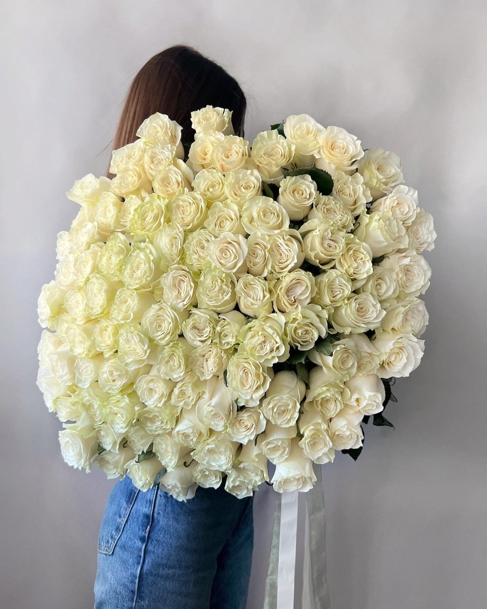 Large bouquet of 101 cream white roses held by woman in blue jeans against gray background