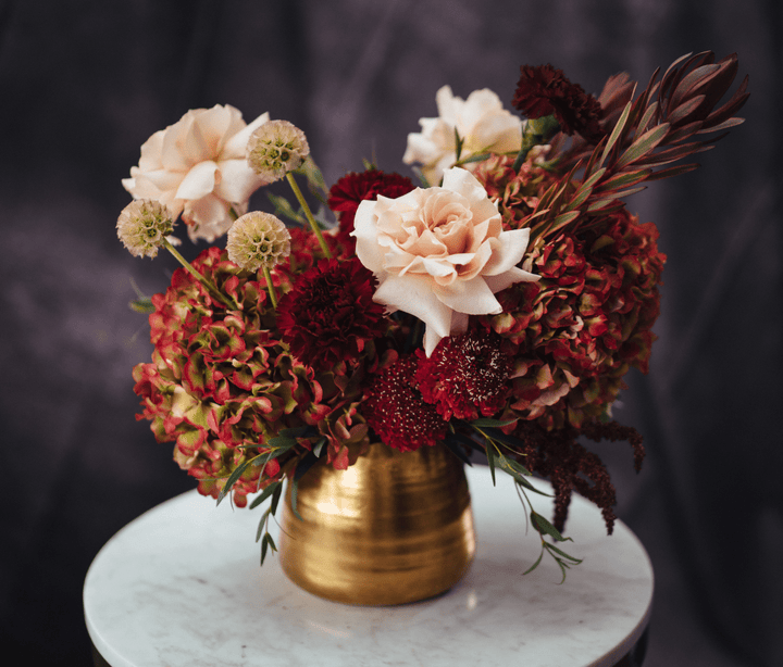 Floral arrangement in a gold vase on a marble surface with a dark background