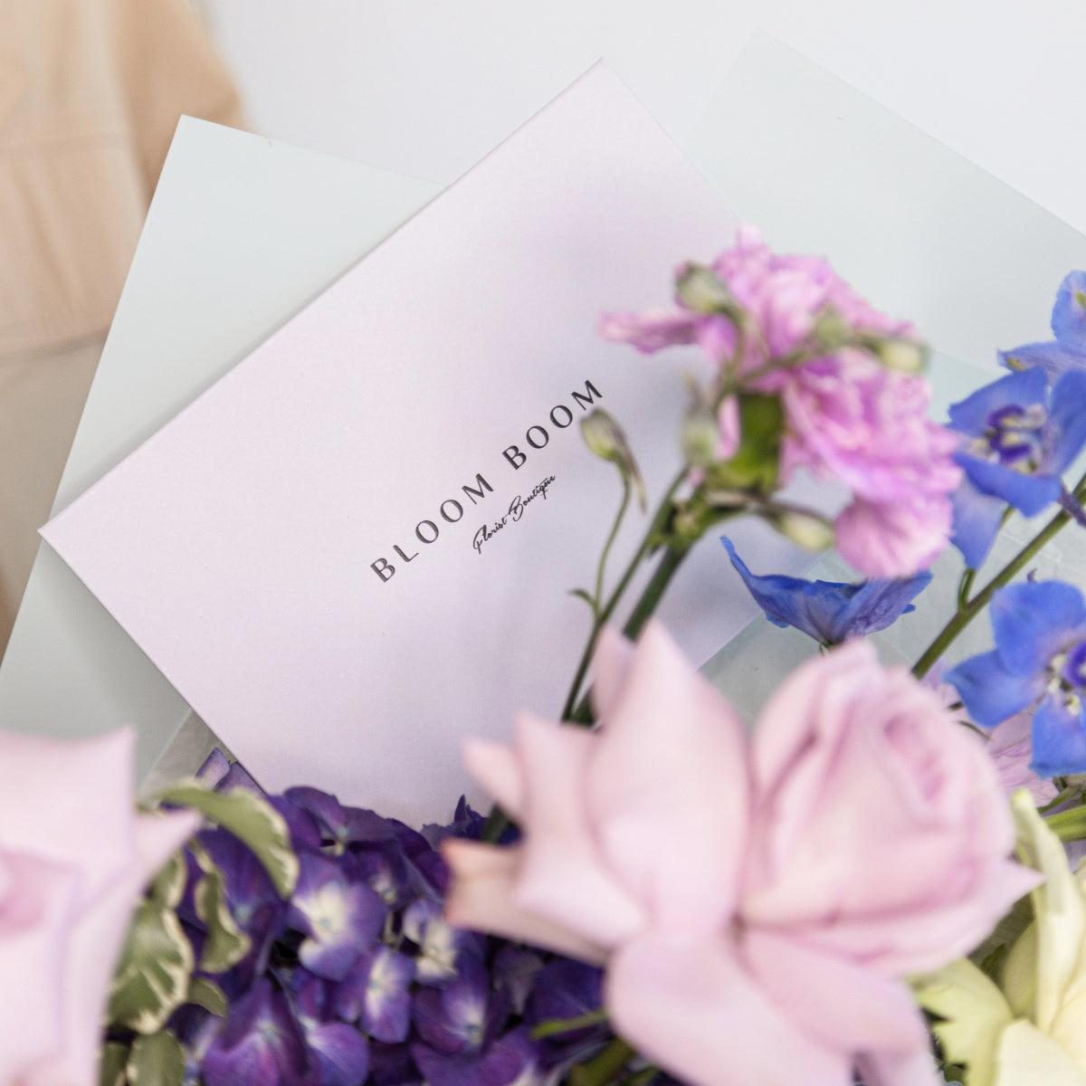 Bloom Boom branded card nestled in pink roses and blue delphinium flower bouquet arrangement