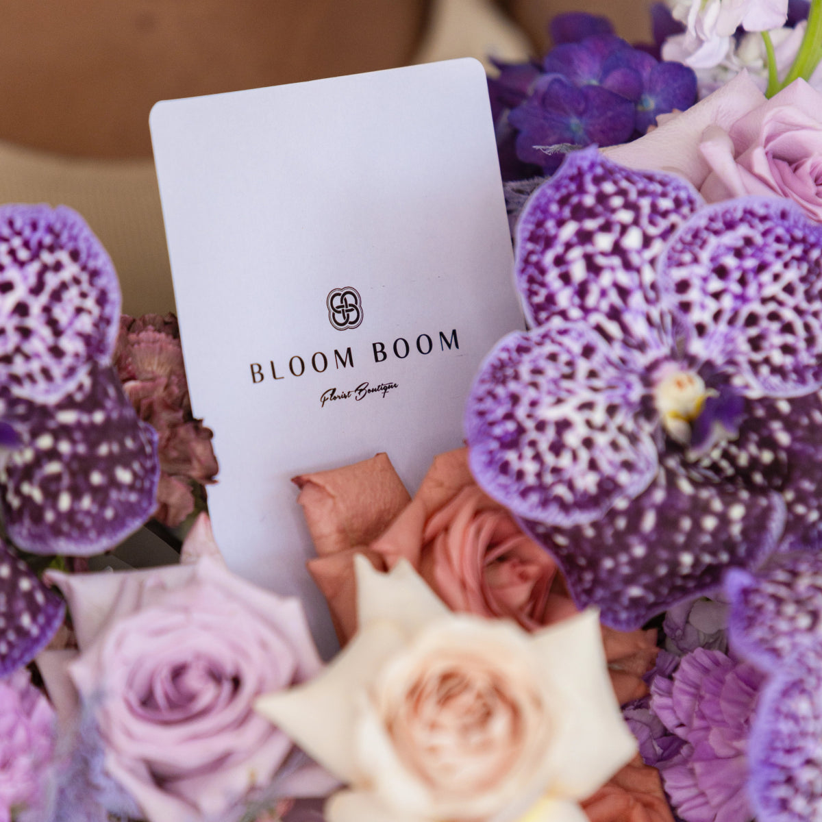 White Bloom Boom card nestled in purple spotted orchids, lavender roses, and coral flowers arrangement