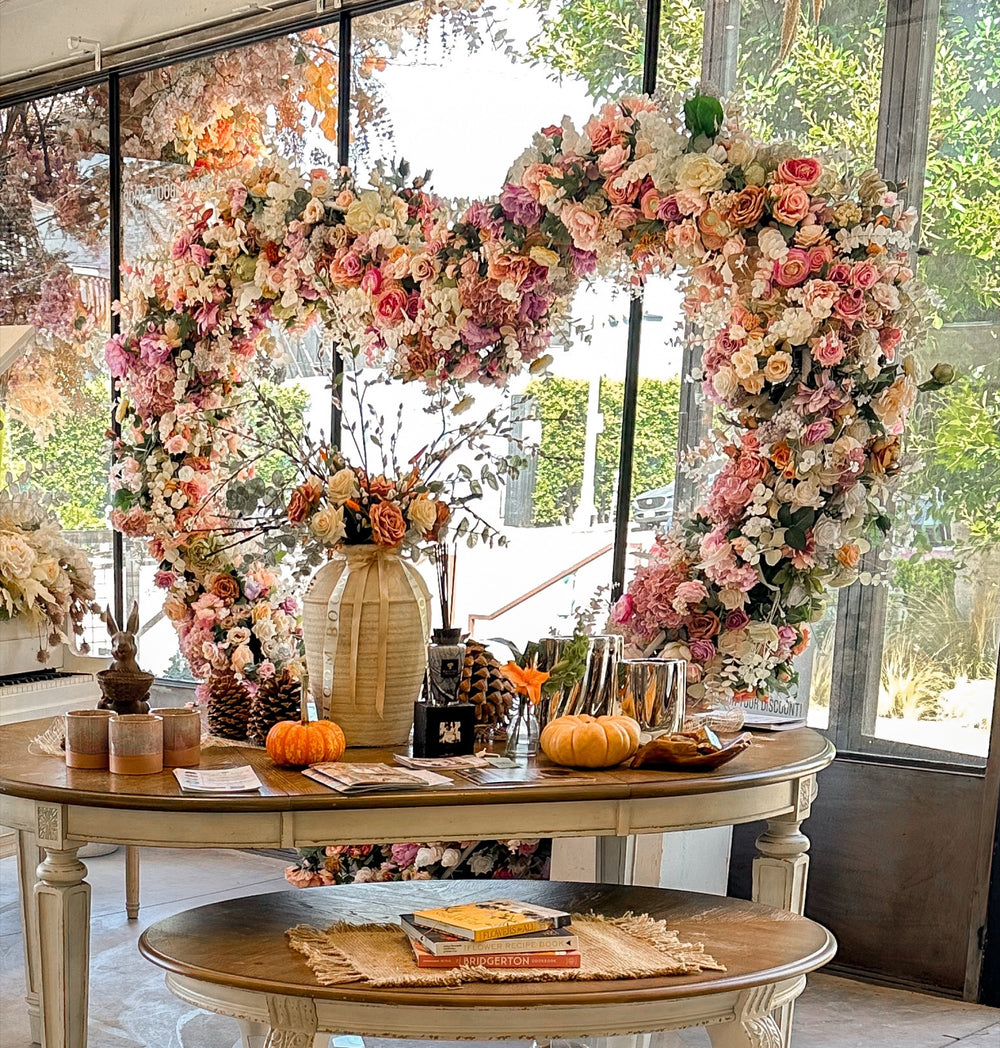 Oversized floral heart arch in blush and peach roses framing the front window above styled tables