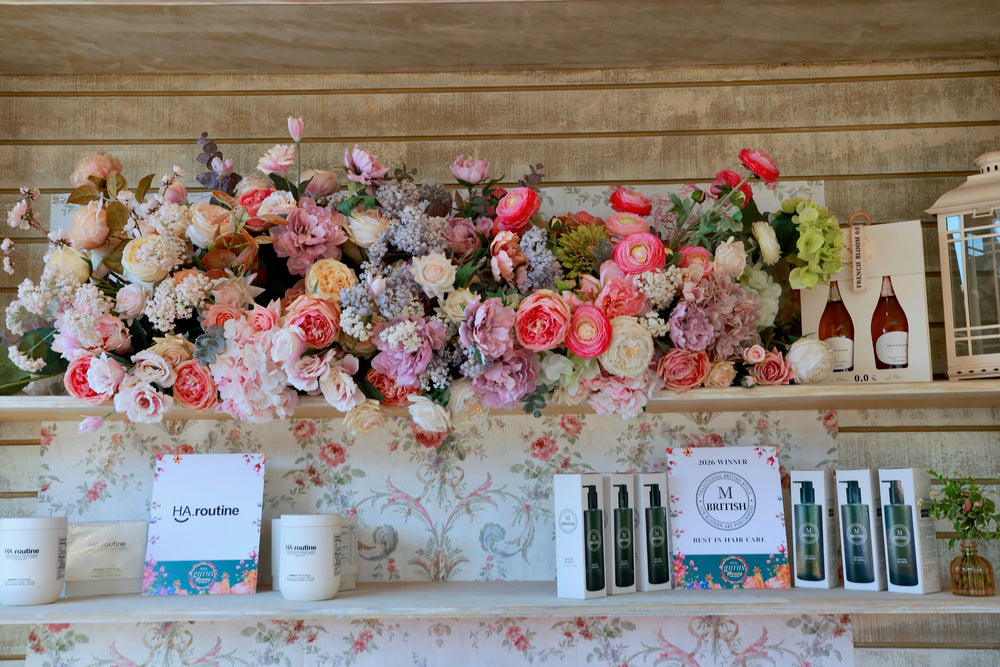 Beauty product display shelf beneath a garland of peonies, roses and ranunculus