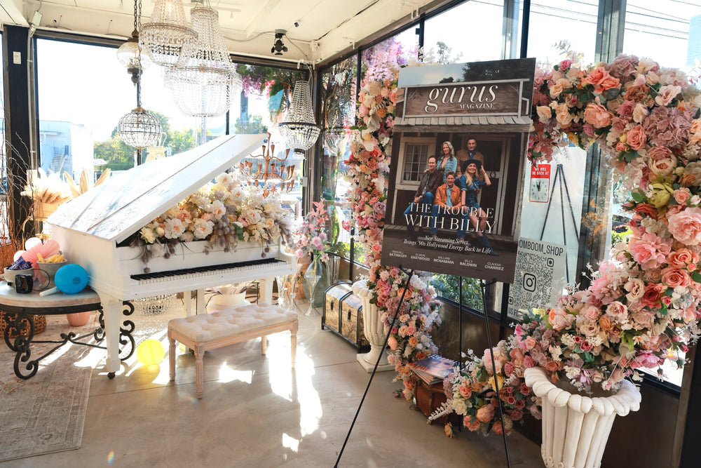 White grand piano and floral heart arch styled beside the premiere poster under crystal chandeliers