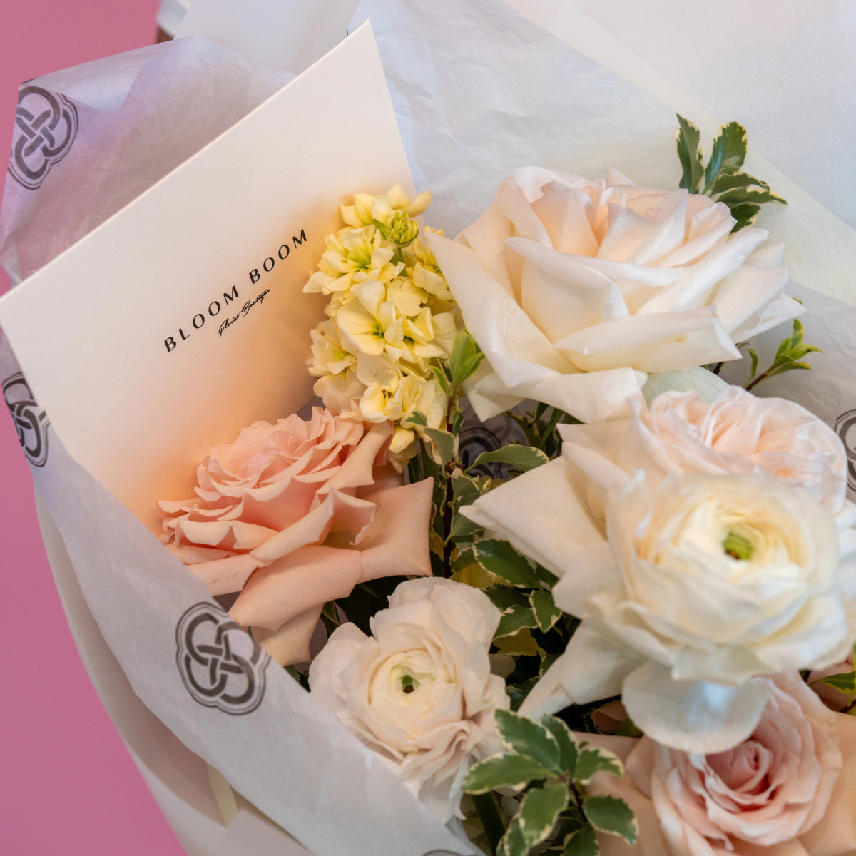 Bloom Boom branded bouquet with white and blush pink roses, ranunculus, and yellow flowers in white paper wrapping