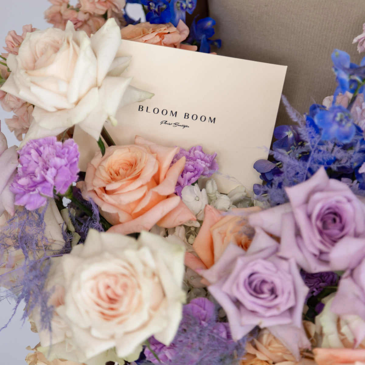 Bloom Boom floral bouquet with peach, purple and white roses, carnations and blue delphiniums with cream ribbon