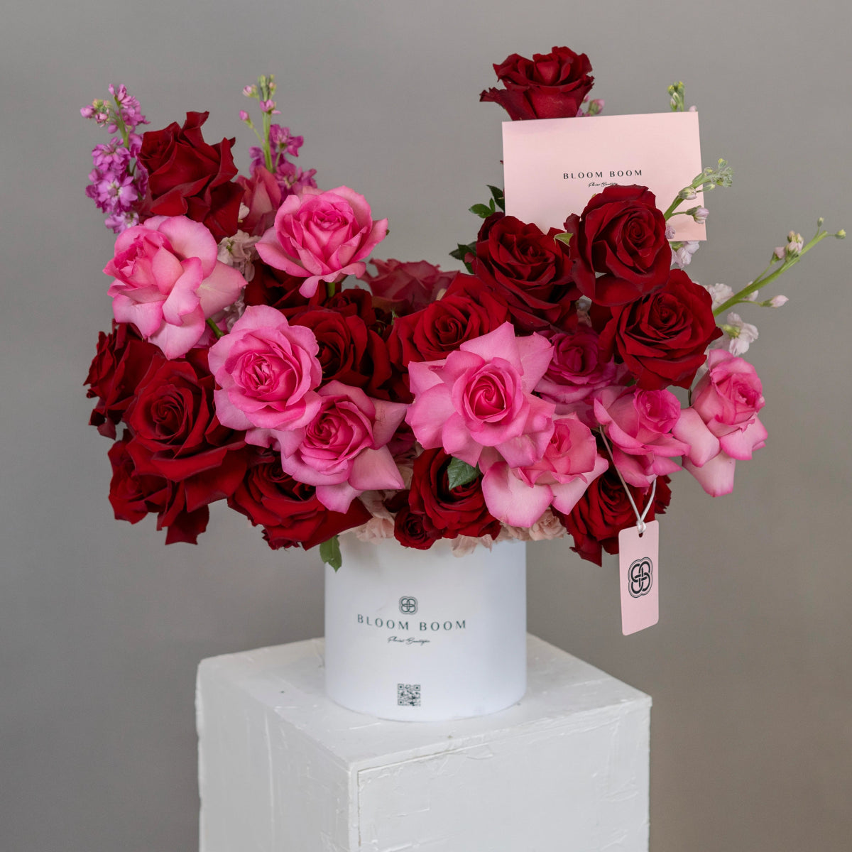 Luxury mixed rose bouquet in white cylinder box with deep red and bright pink roses, purple stock flowers
