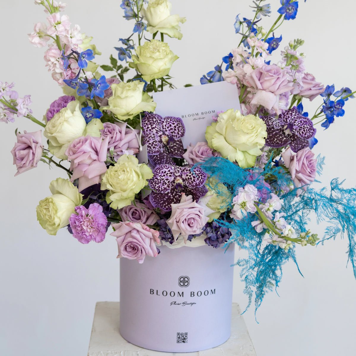 Luxury flower arrangement in lavender box with purple roses, white roses, blue delphinium, and turquoise orchids