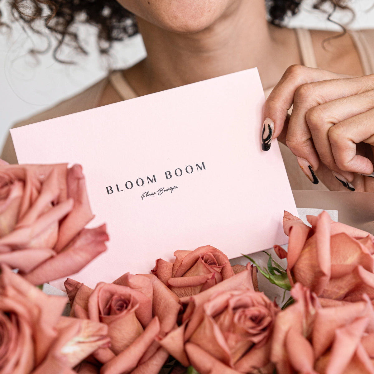 Woman holding pink Bloom Boom card with dusty rose flowers and black manicured nails in elegant bouquet setting