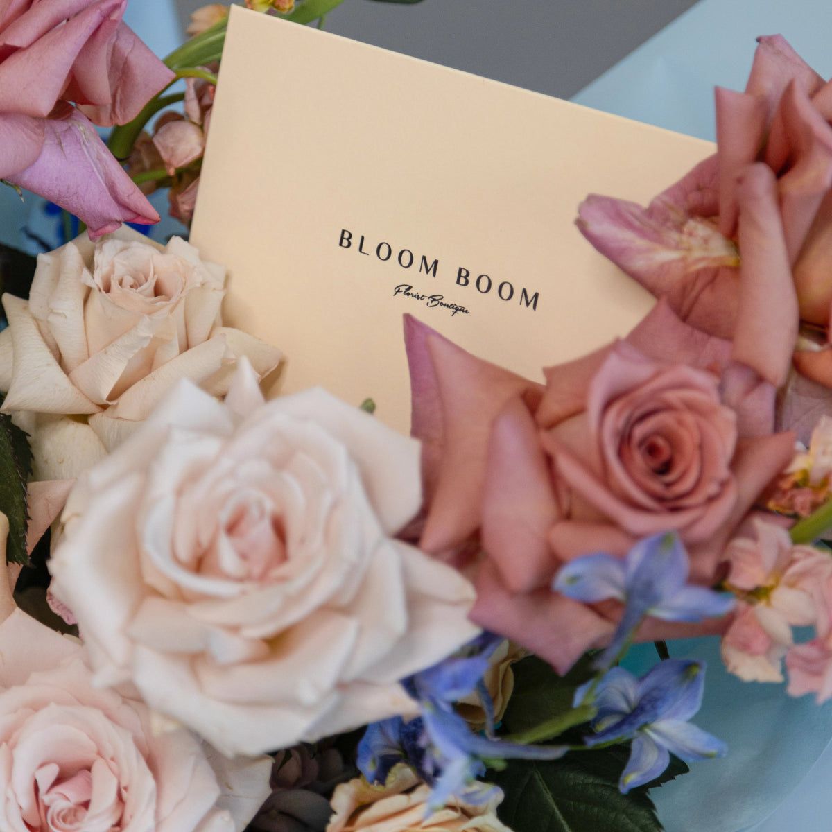 Bloom Boom flower bouquet with blush pink roses, white roses and blue delphinium with cream business card