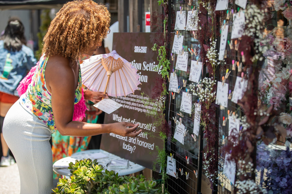 Guest pinning a handwritten card to the flower-lined intention-setting wall on the patio