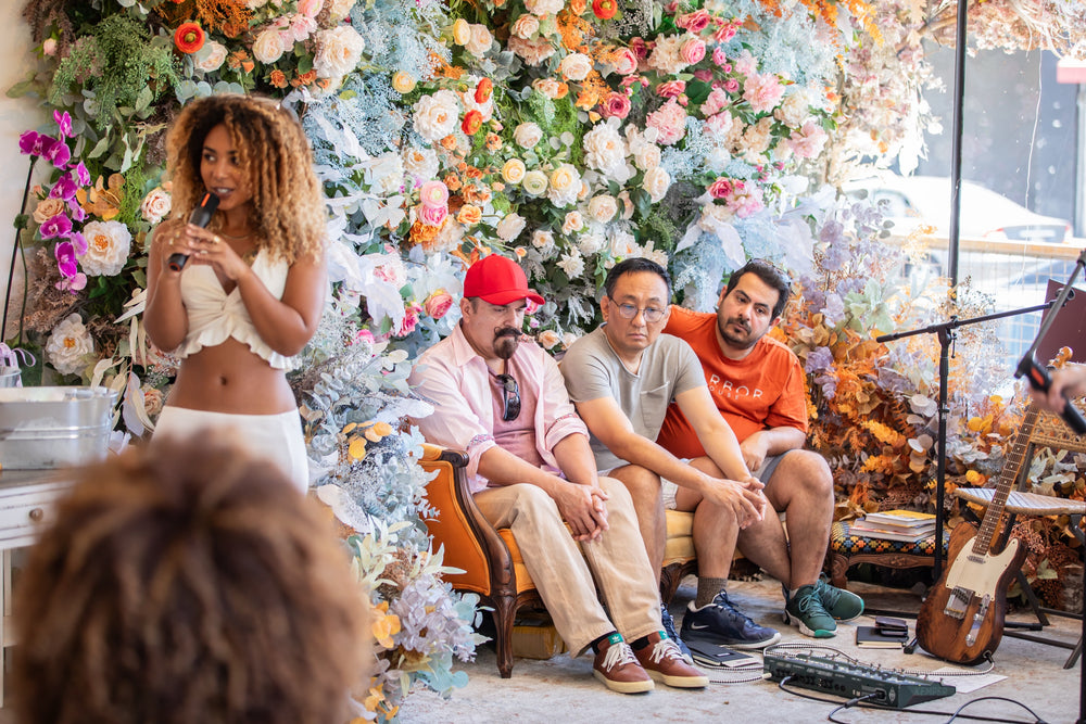 Speaker with a microphone leading a panel conversation with guests seated on the orange velvet sofa against the floral wall