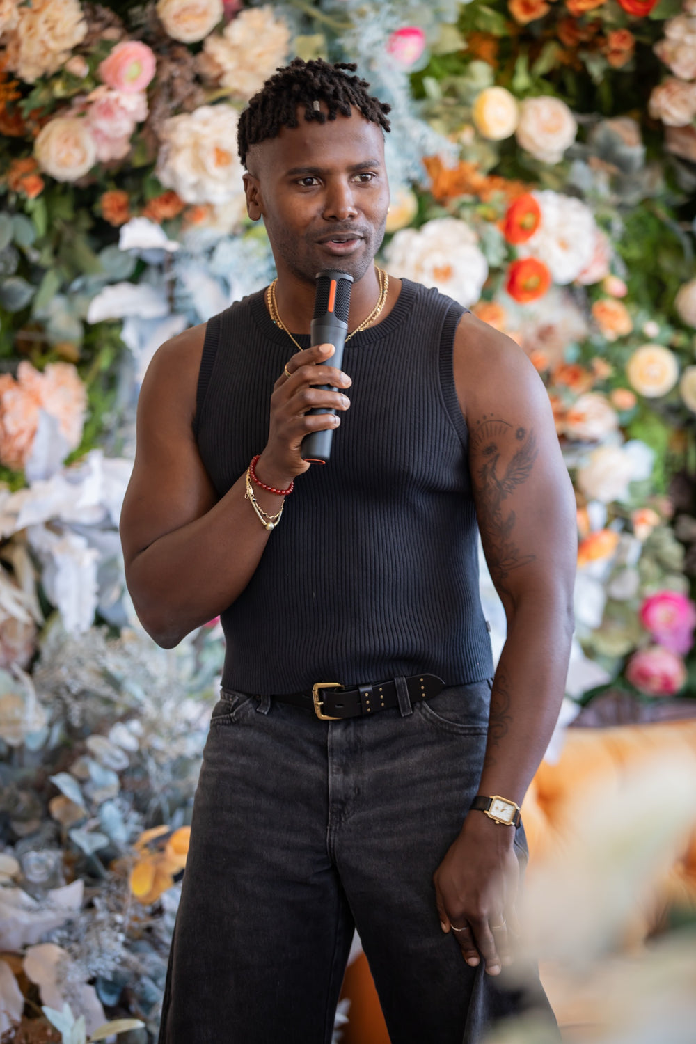 Speaker addressing guests with a microphone in front of the coral and peach floral wall