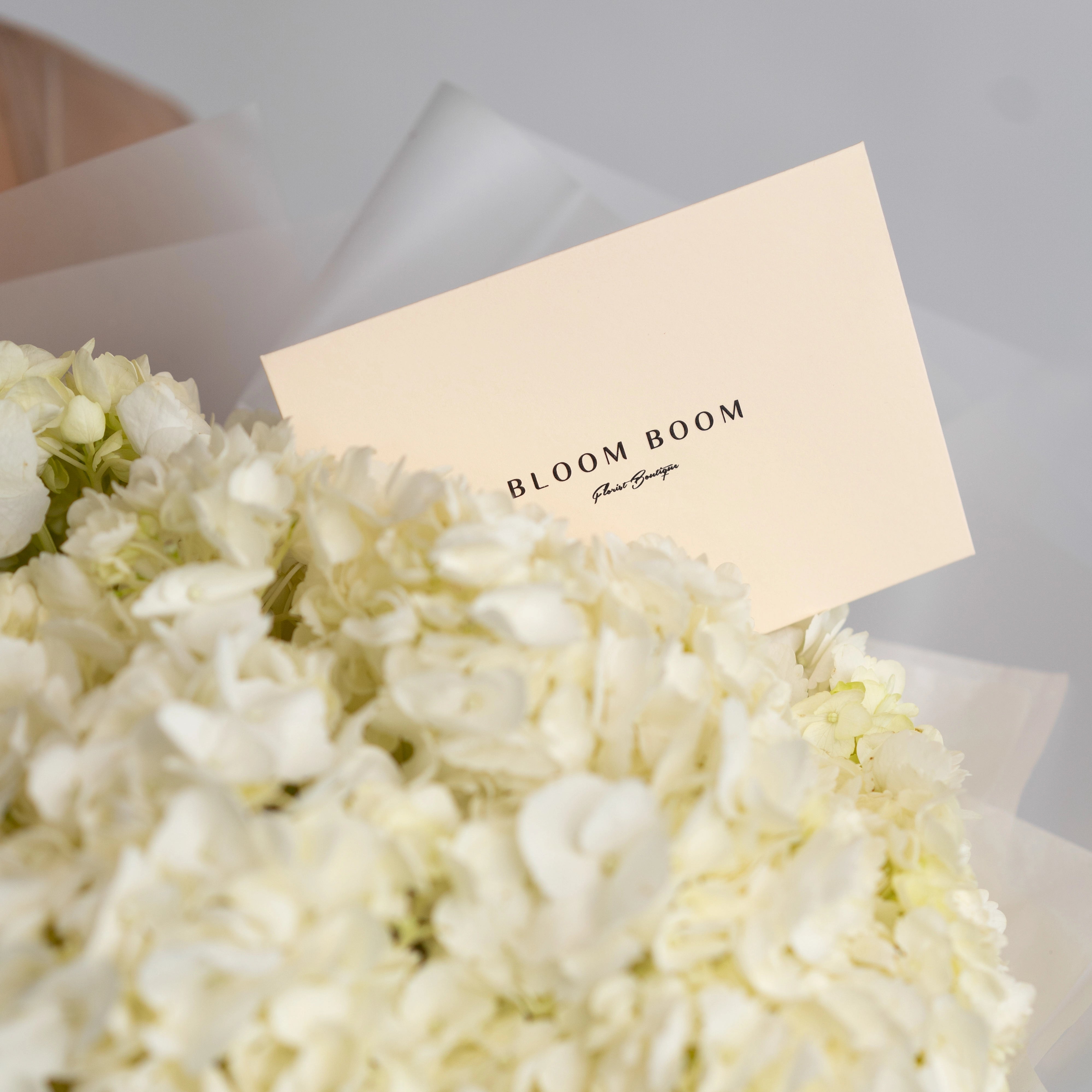 White hydrangea bouquet with Bloom Boom Flower Boutique business card featuring elegant branding design