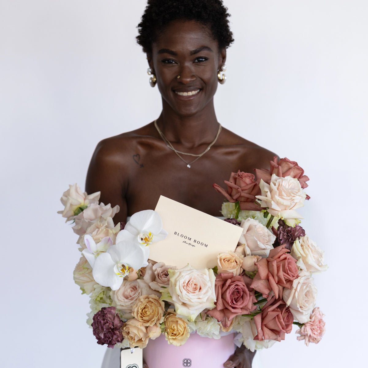 Luxury flower arrangement in pink box with blush roses, white orchids, and purple blooms held by smiling woman