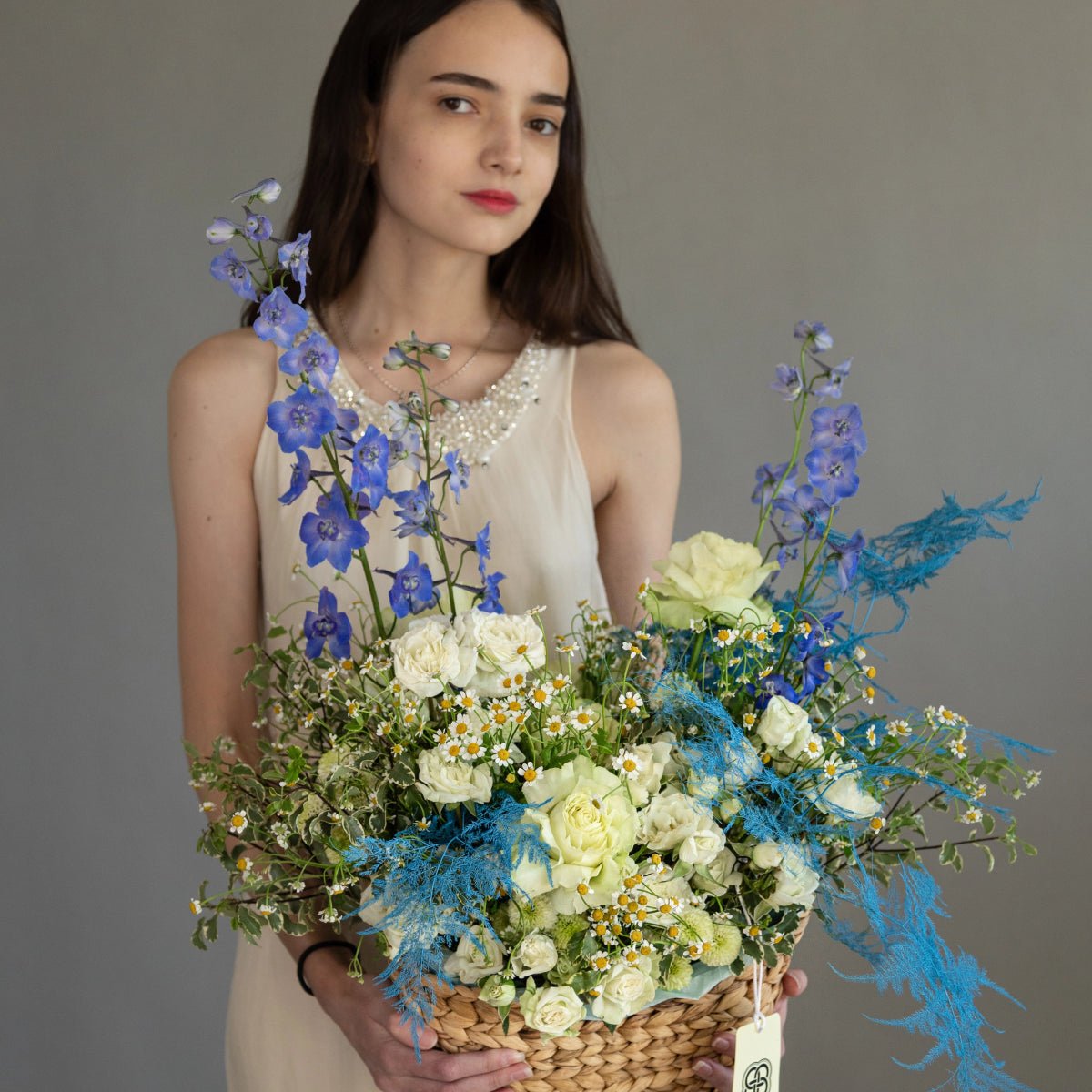 Blue summer flower basket with white roses, blue delphinium, chamomile daisies and turquoise dried grass in wicker