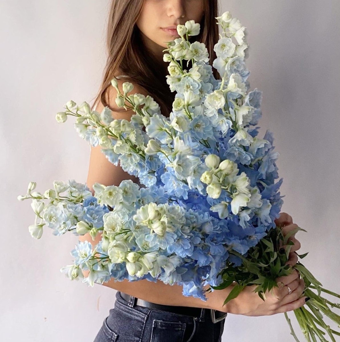 Large blue and white delphinium flower bouquet with tall spiky blooms held by woman in casual outfit