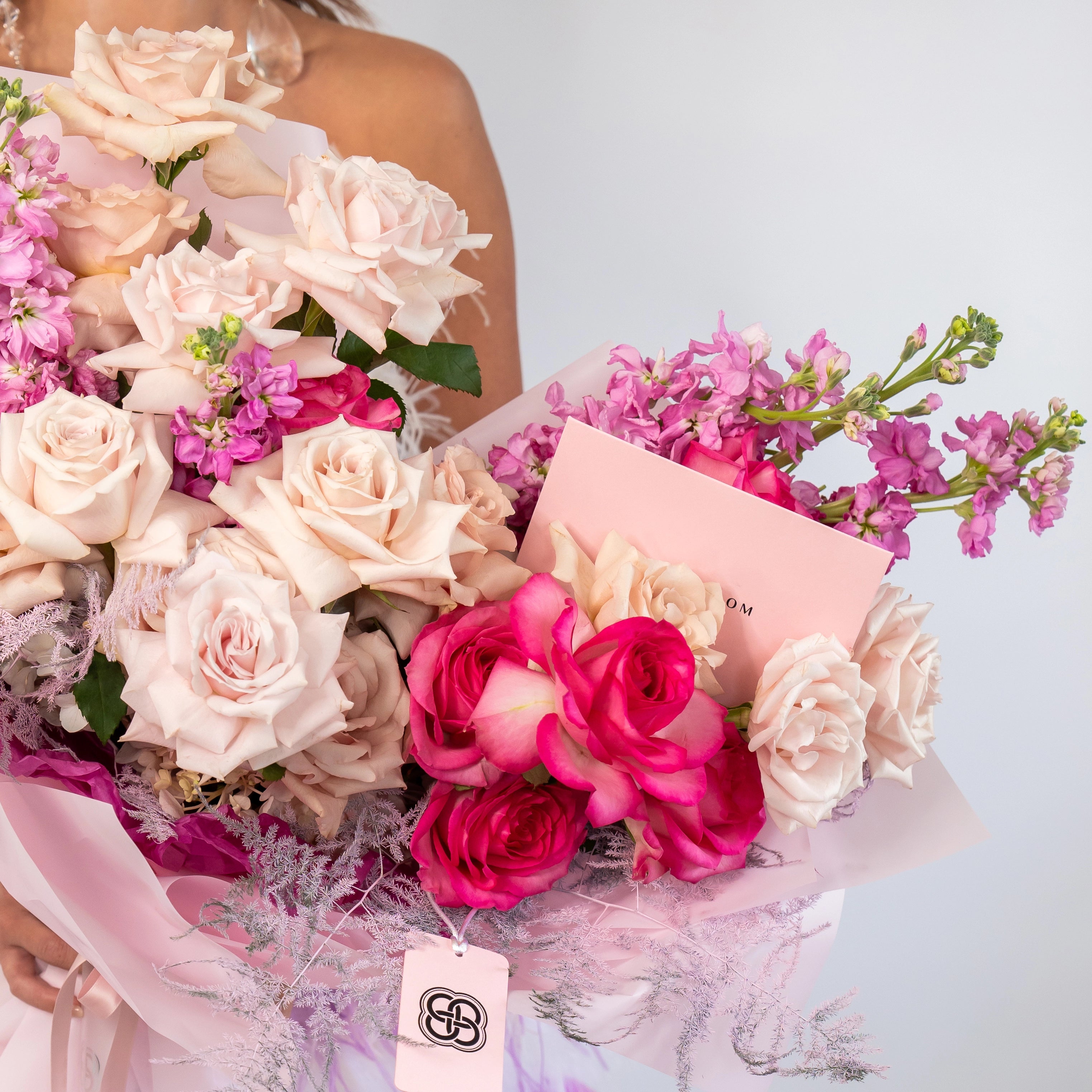 Elegant bouquet with blush pink roses, hot pink roses, and purple stock flowers wrapped in pink paper