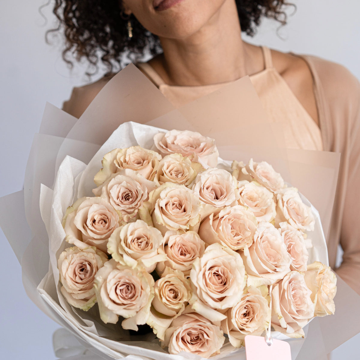 Luxurious bouquet of blush pink quicksand roses wrapped in white paper held by woman in beige dress