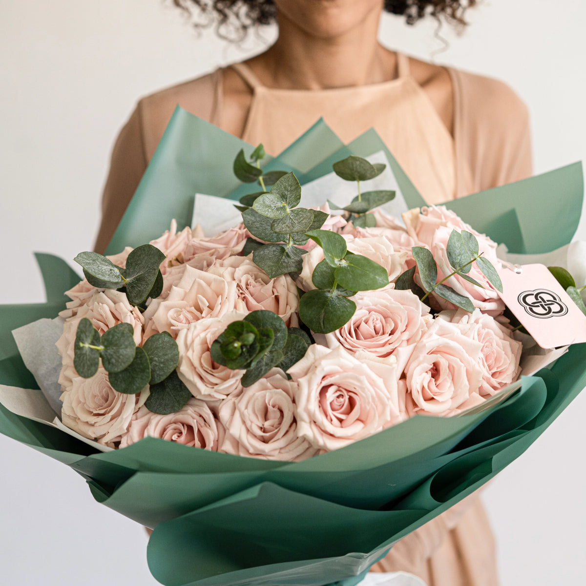 Blush pink rose bouquet with eucalyptus leaves wrapped in sage green paper, held by woman in peach dress
