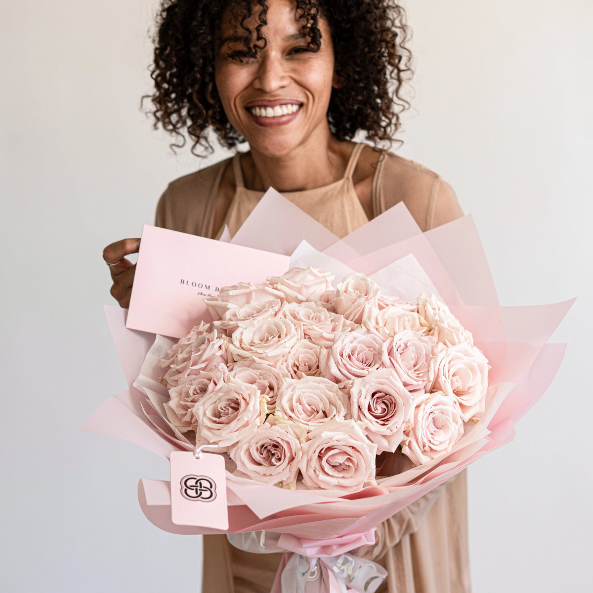 Smiling woman holding luxury bouquet of 25 blush pink roses wrapped in soft pink paper with ribbon