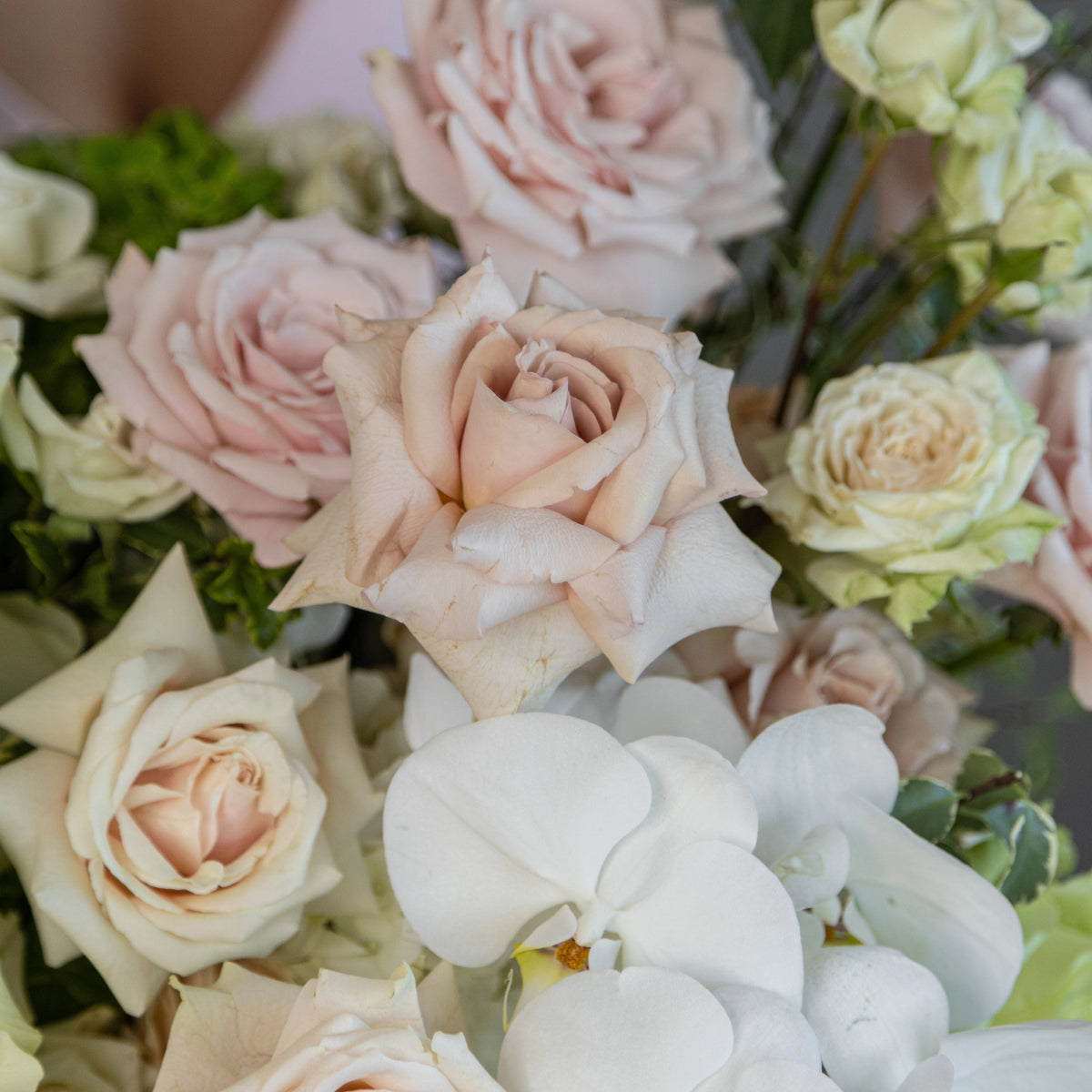 Blush pink roses, white orchids and cream roses arranged in elegant mixed flower bouquet with green foliage
