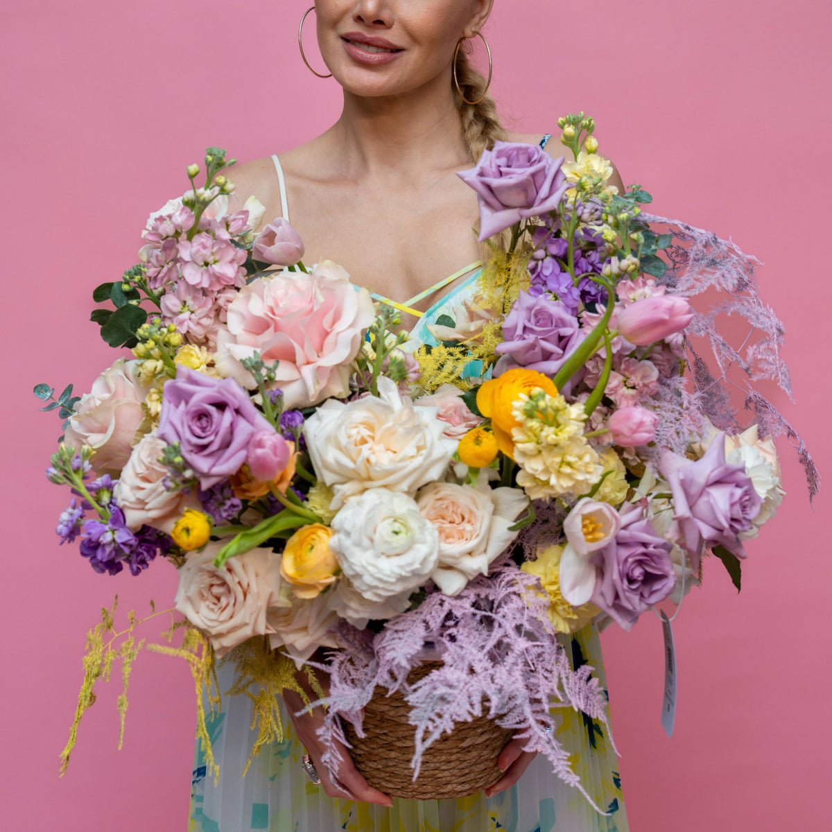 Colorful flower bouquet in wicker basket with purple roses, pink ranunculus, yellow blooms and dusty miller foliage