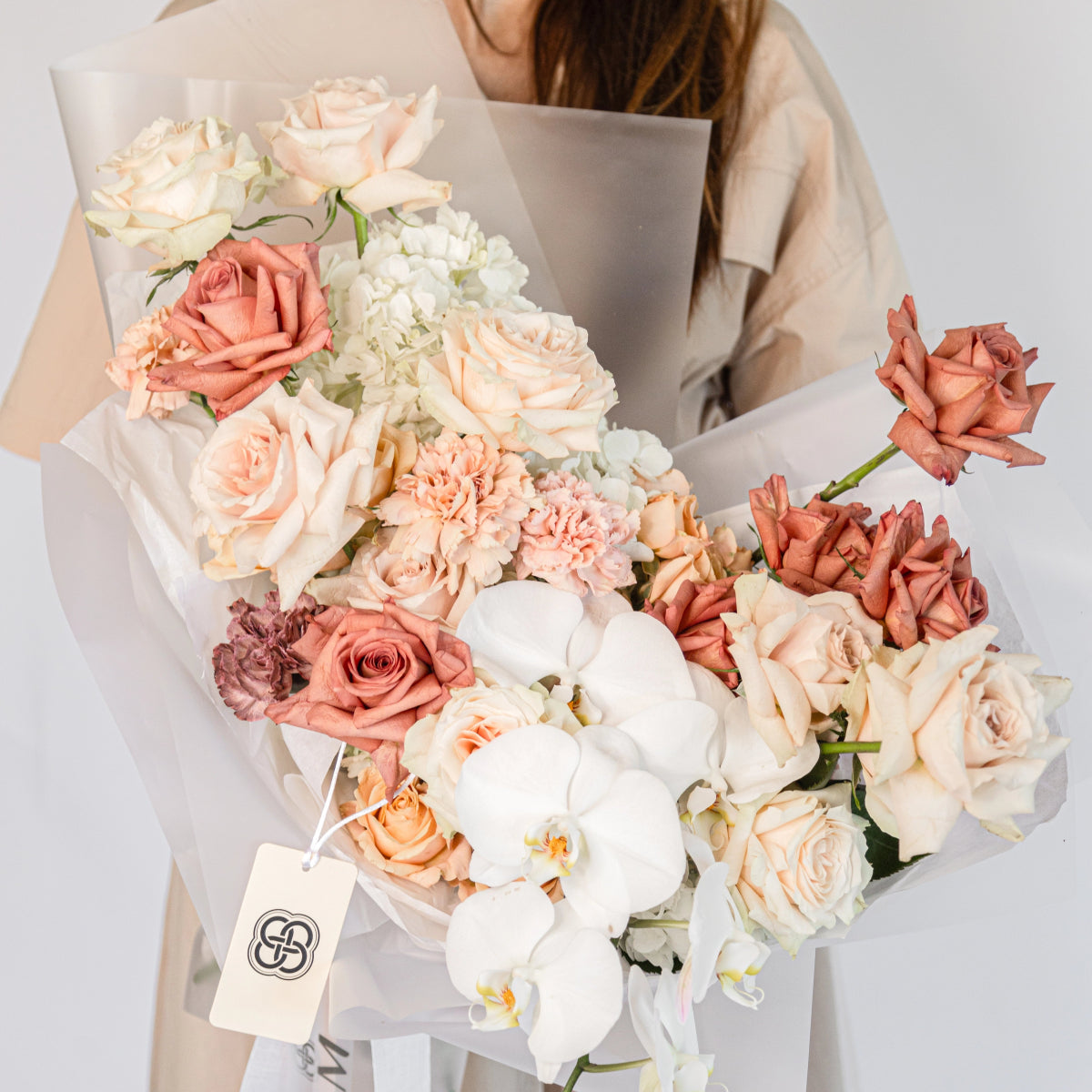 Elegant mixed flower bouquet with coral roses, white orchids, pink carnations and hydrangea in cream paper wrapping