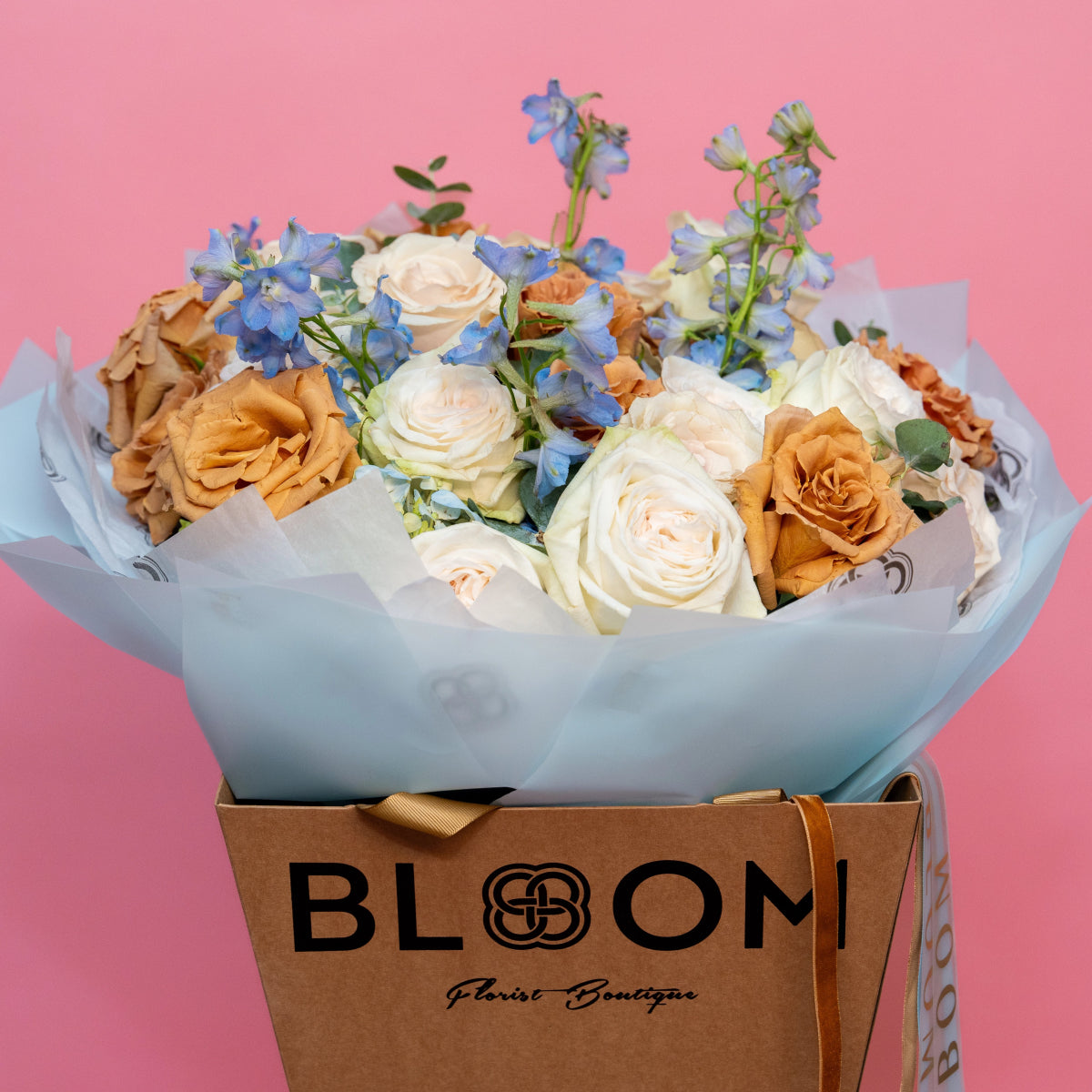 Mixed flower bouquet with cream roses, orange roses and blue delphinium in white paper wrapped in BLOOM branded box