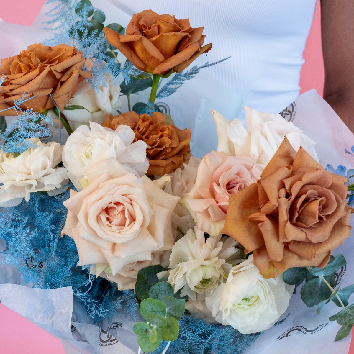 Cappuccino bouquet with peach roses, white ranunculus, blue dusty miller wrapped in tissue paper